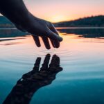 Finger touches surface of mountain lake. Hand reflection